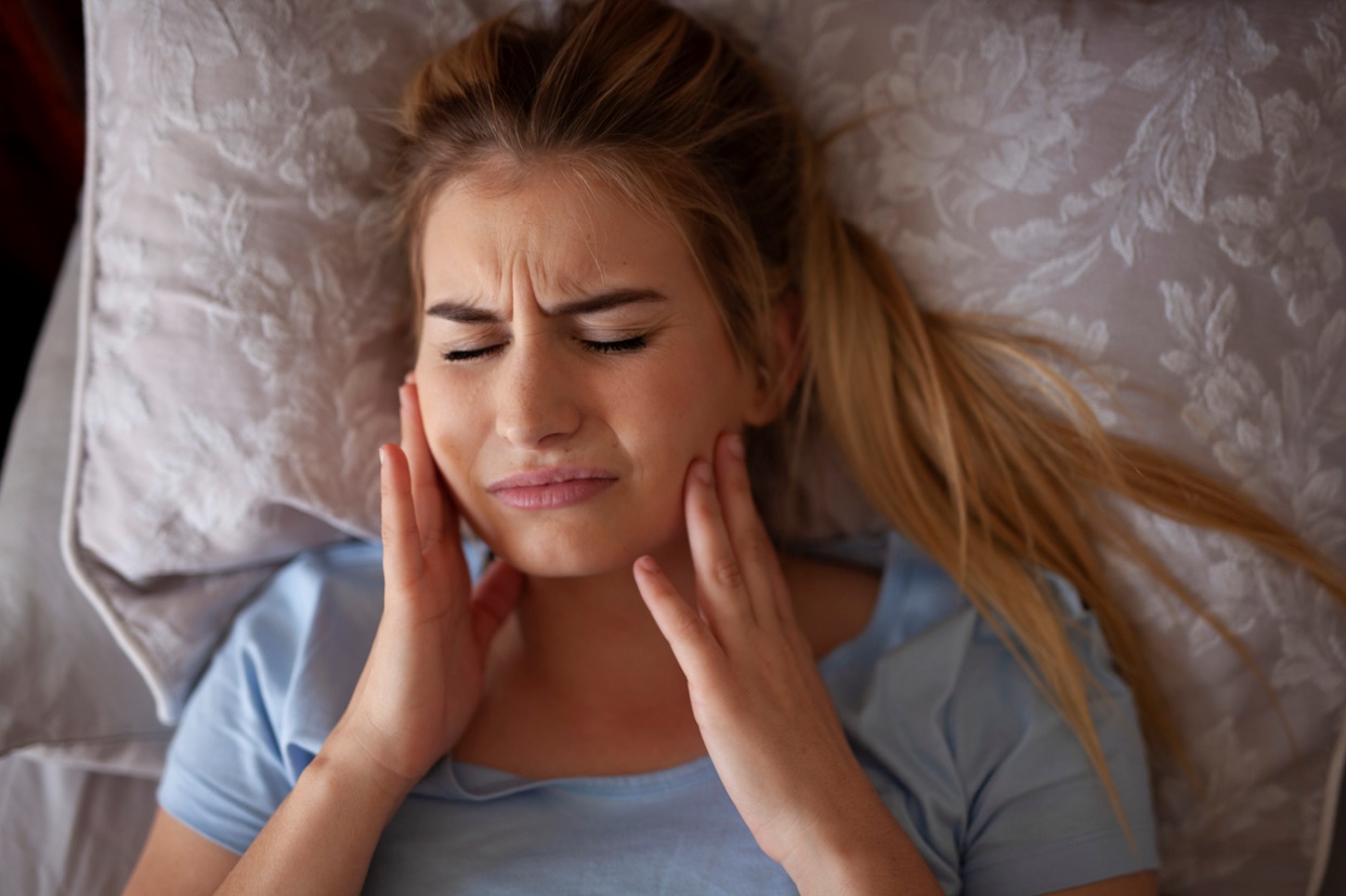 Understanding Jaw Pain: TMJ Disorder and How to Find Relief, A woman laying in her bed with ther hands on her jaw in pain